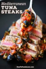 A close-up view of a person spooning a sauce of tomatoes, black olives and capers over sliced Mediterranean tuna steaks.