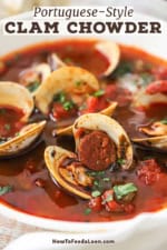 A close-up view of a white bowl filled with a serving of Portuguese-style clam chowder with pieces of cooked chorizo, tomato chunks, and opened littleneck clams visible.