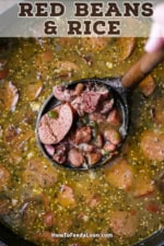 An overhead view of a person lifting a large wooden ladle out of a pot filled with a thick broth, course-ground mustard, red kidney beans, and smoked sausage and ham.