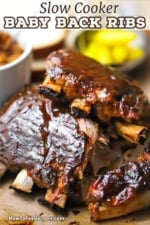 Two half-racks of slow cooker baby back ribs stacked on top of each other and with barbecue sauce smear over the tops of each rack.