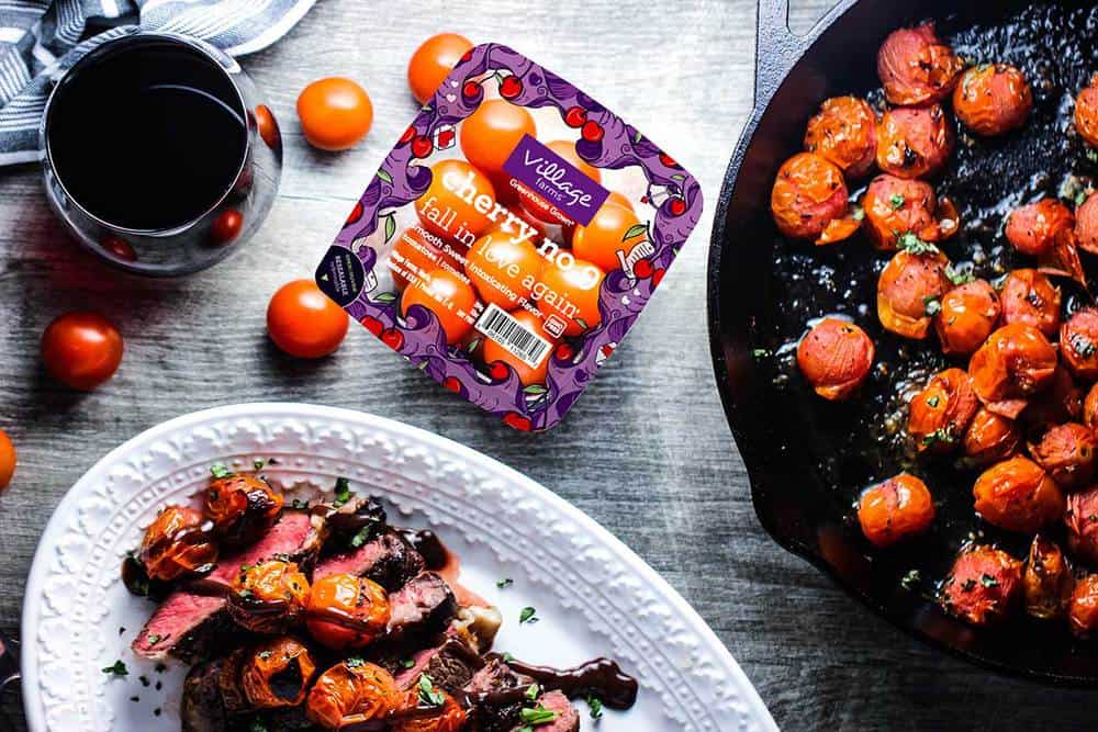 Seared ribeye with blistered tomatoes and bordelaise sauce on a platter next to a cast iron skillet of tomatoes