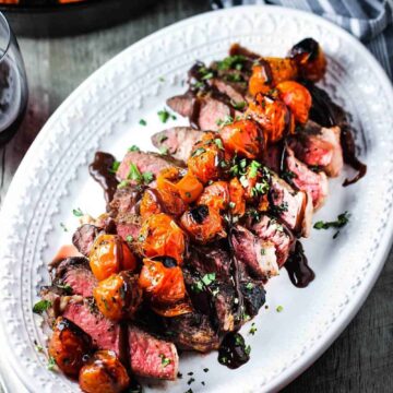 Sliced ribeye steak on a platter with roasted tomatoes and borderalaise sauce