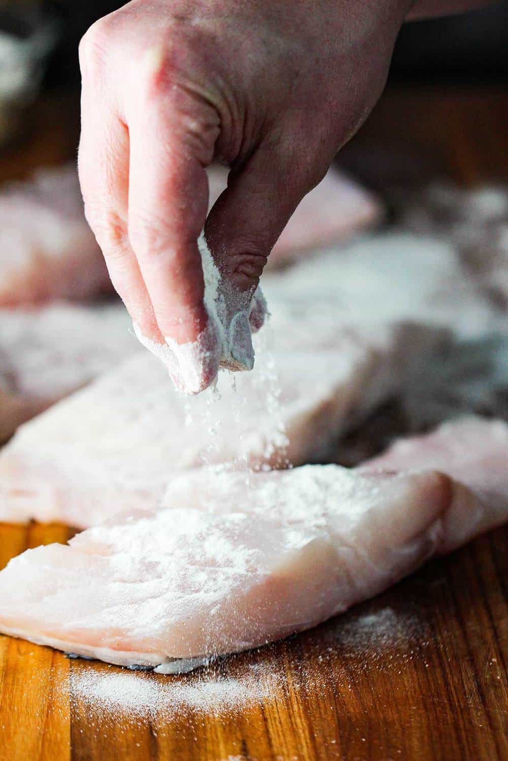 Fingers dusting flour over fresh wild striped bass fillets