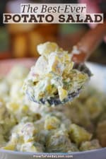 A person raising a wooden spoon filled with a serving of best-ever potato salad over a bowl of the same.