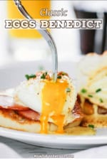 A person using a fork to pierce open a poached egg with a runny yolk spilling over the sides of an Eggs Benedict.