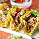 A white platter with three Carnitas Tacos