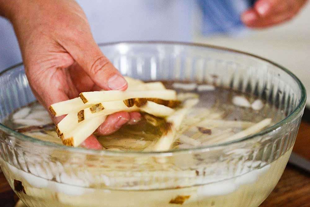 A hand holding cut potatoes in a bowl of ice water. 