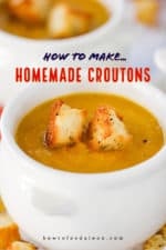 A white crock holding butternut squash soup with two homemade croutons on top.
