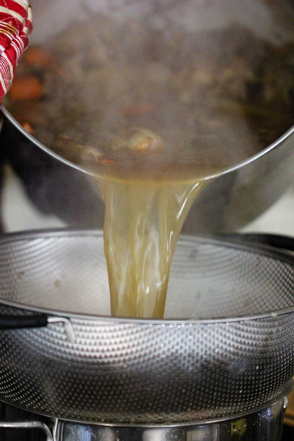 A large stock pan pouring roasted chicken stock into a colander over another pot. 