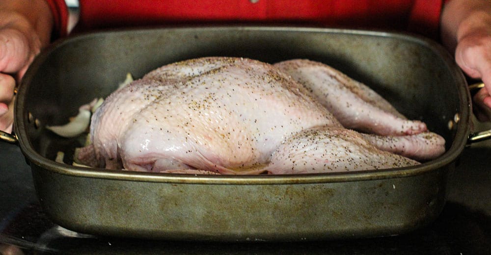 An uncooked spatchcocked turkey in a large roasting pan. 