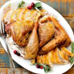 A cooked and carved spatchcocked turkey on a large white platter with a fork next to it.