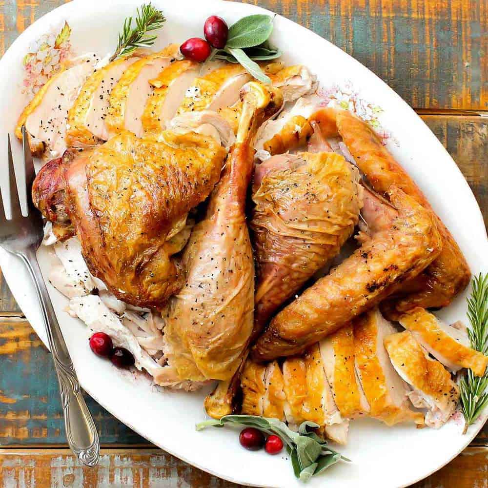 A cooked and carved spatchcocked turkey on a large white platter with a fork next to it. 