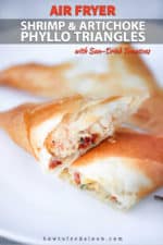 A split open air fryer phyllo triangle stuffed with shrimp and artichokes on a white plate.