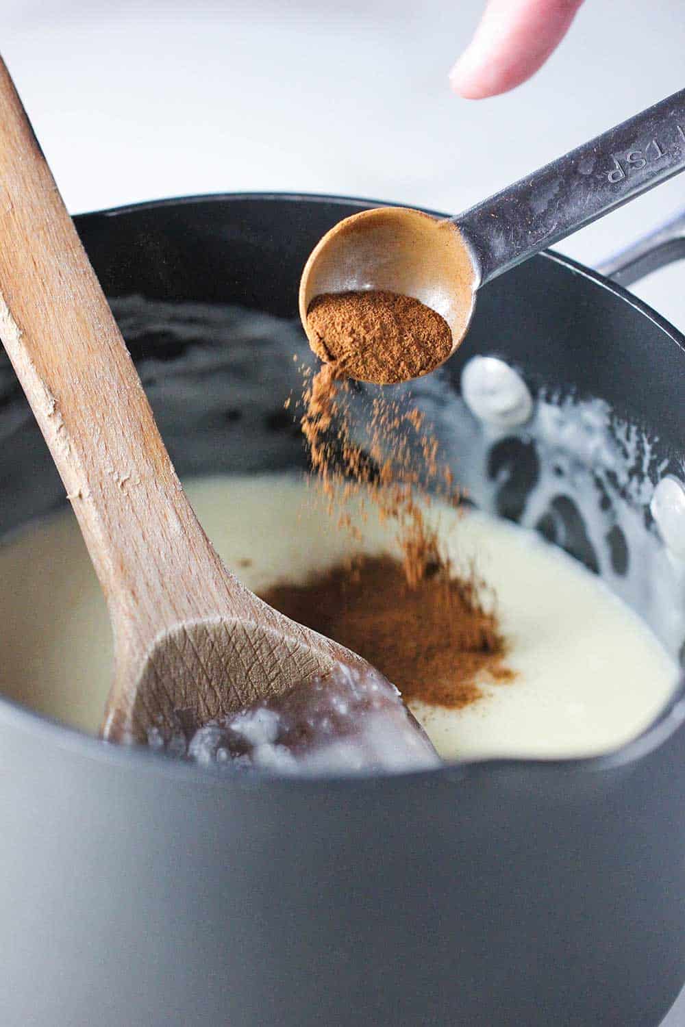 Ground cinnamon being added to a pan of melted white chocolate. 