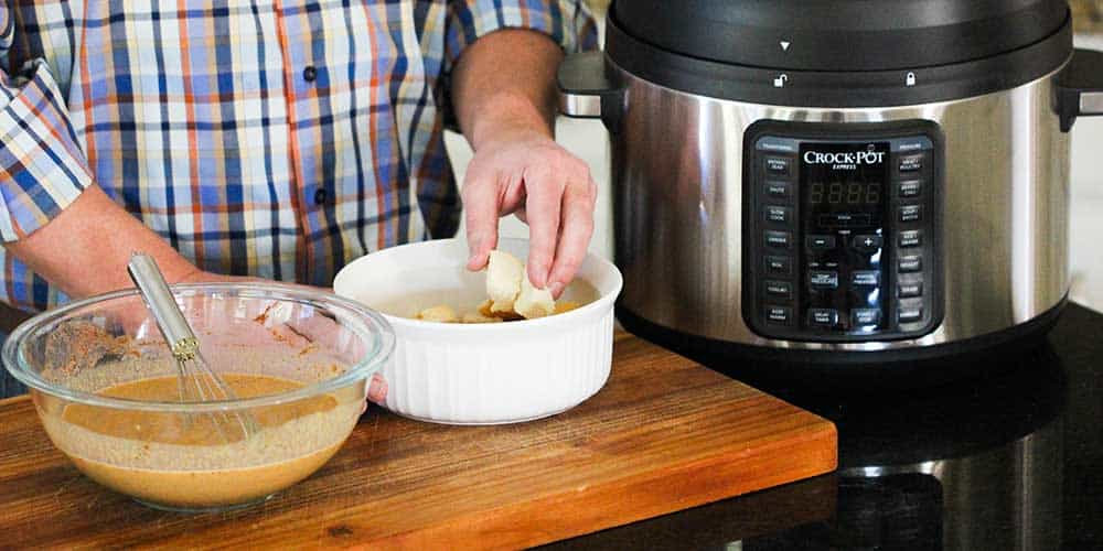 Two hands adding bread pieces into a white bowl next to a Crock-Pot.