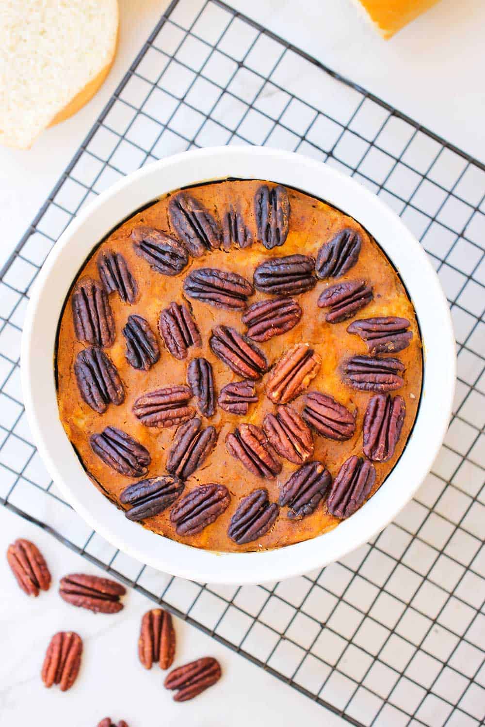 A bowl of pressure cooker pumpkin bread pudding on a baking rack next to pecans. 