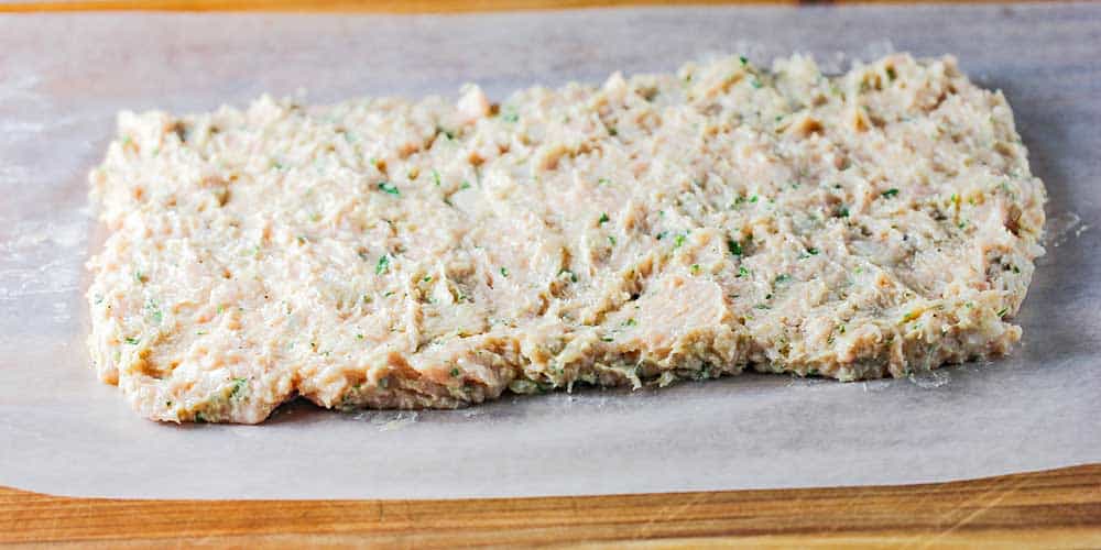 A layer of chicken mixture in a rectangle on a piece of wax paper. 