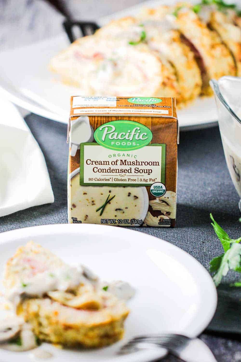 A box of condensed cream of mushroom soup next to a plate and a platter of air fryer cordon bleu meatloaf. 