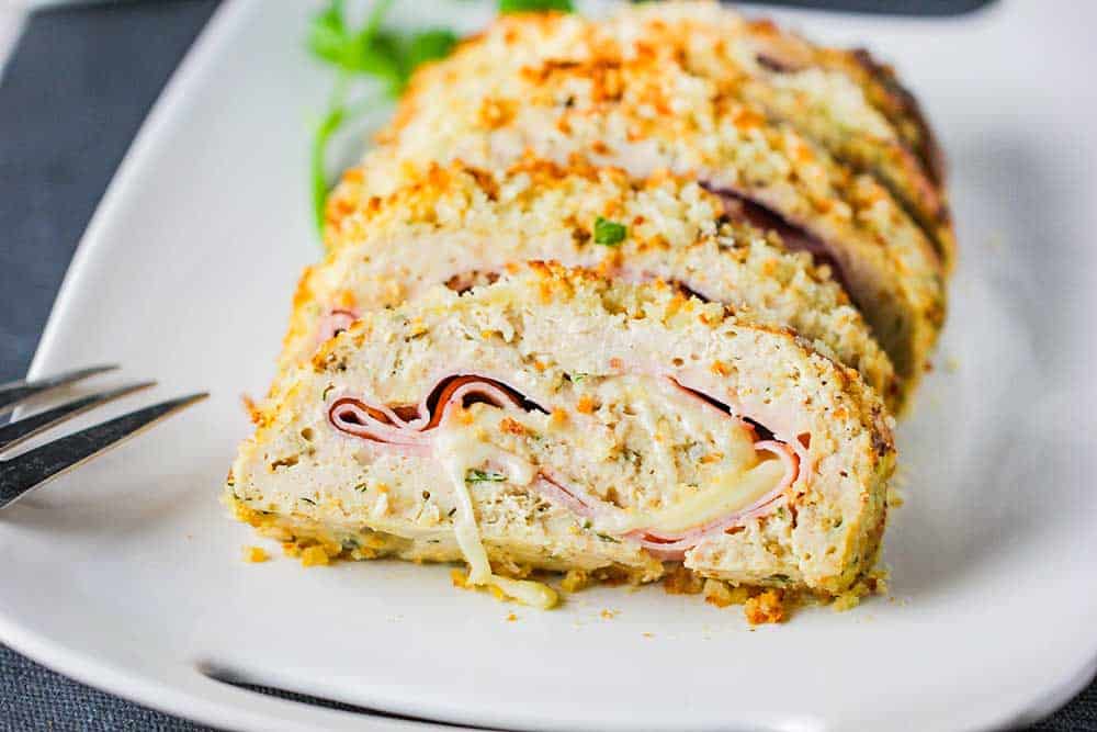 A white platter holding sliced air fryer cordon bleu meatloaf on it with a fork nearby. 