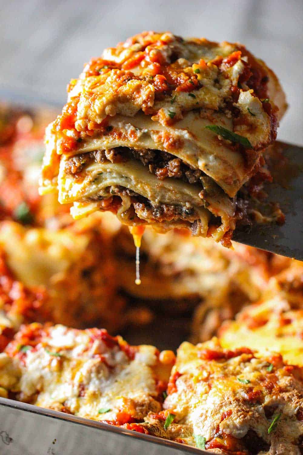 A spatula lifting a piece of classic meat lasagna from a lasagna pan filled with lasagna. 
