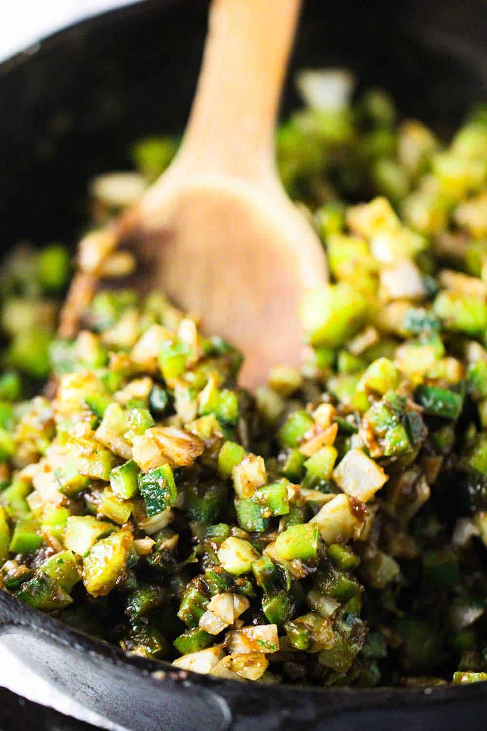 A large wooden spoon stirring vegetables in a cast iron skillet. 