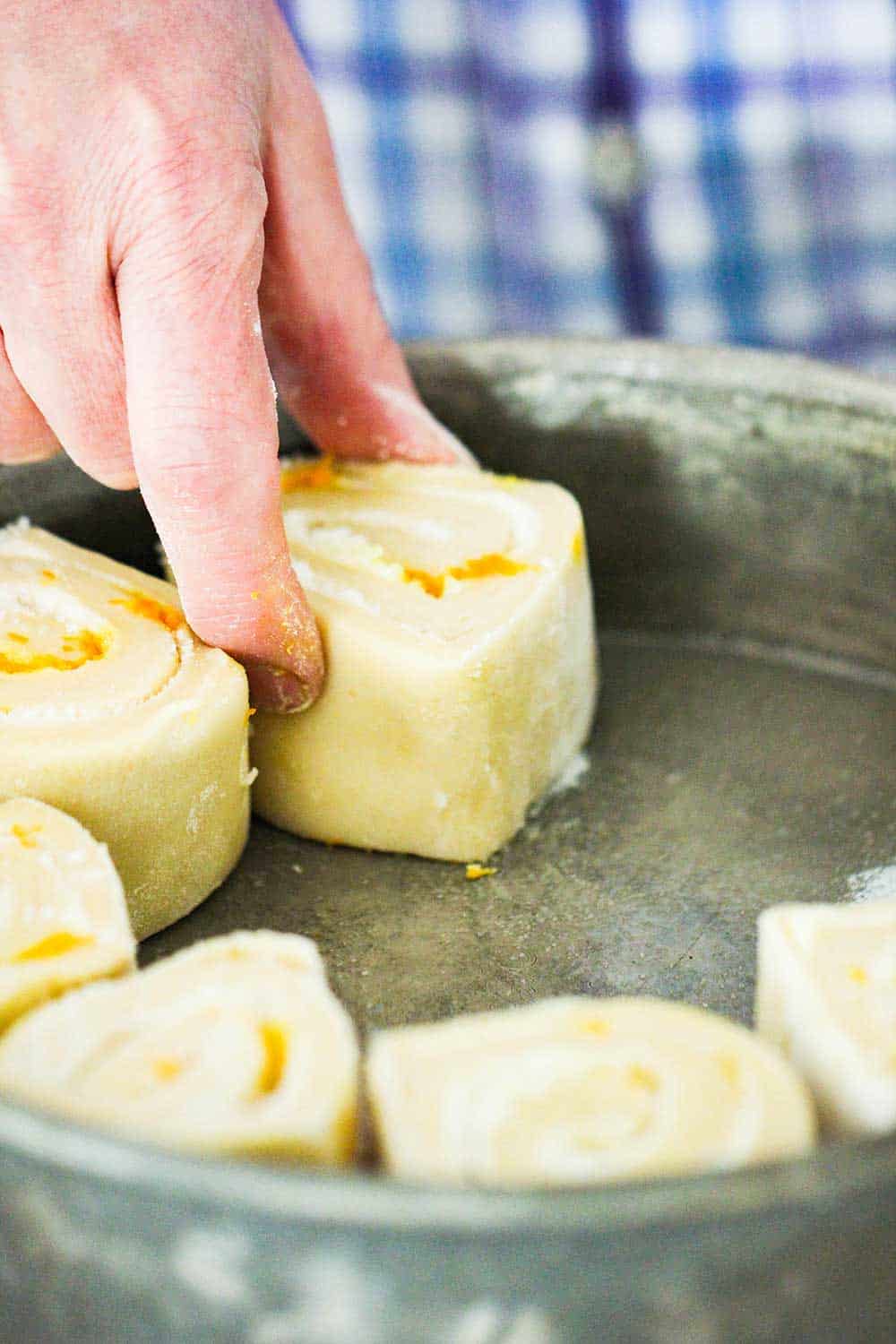 A hand placing an uncooked orange sweet roll into a circular pan.