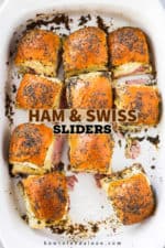 An overhead view of a white baking dish filled with ham and Swiss sliders with one missing.