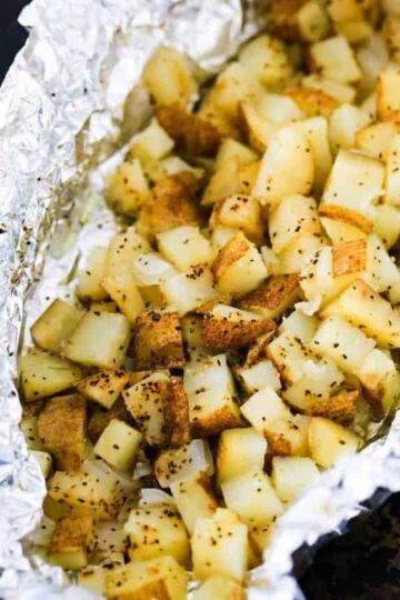 A foil packet filled with cubed roasted potatoes in foil on a baking pan.