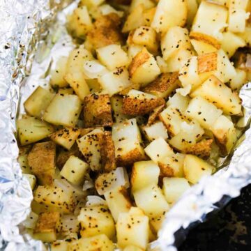 A foil packet filled with cubed roasted potatoes in foil on a baking pan.
