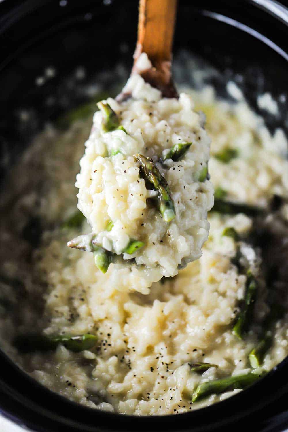 A large wooden spoon filled with slow cooker asparagus risotto being lifted out of the Crock-Pot. 