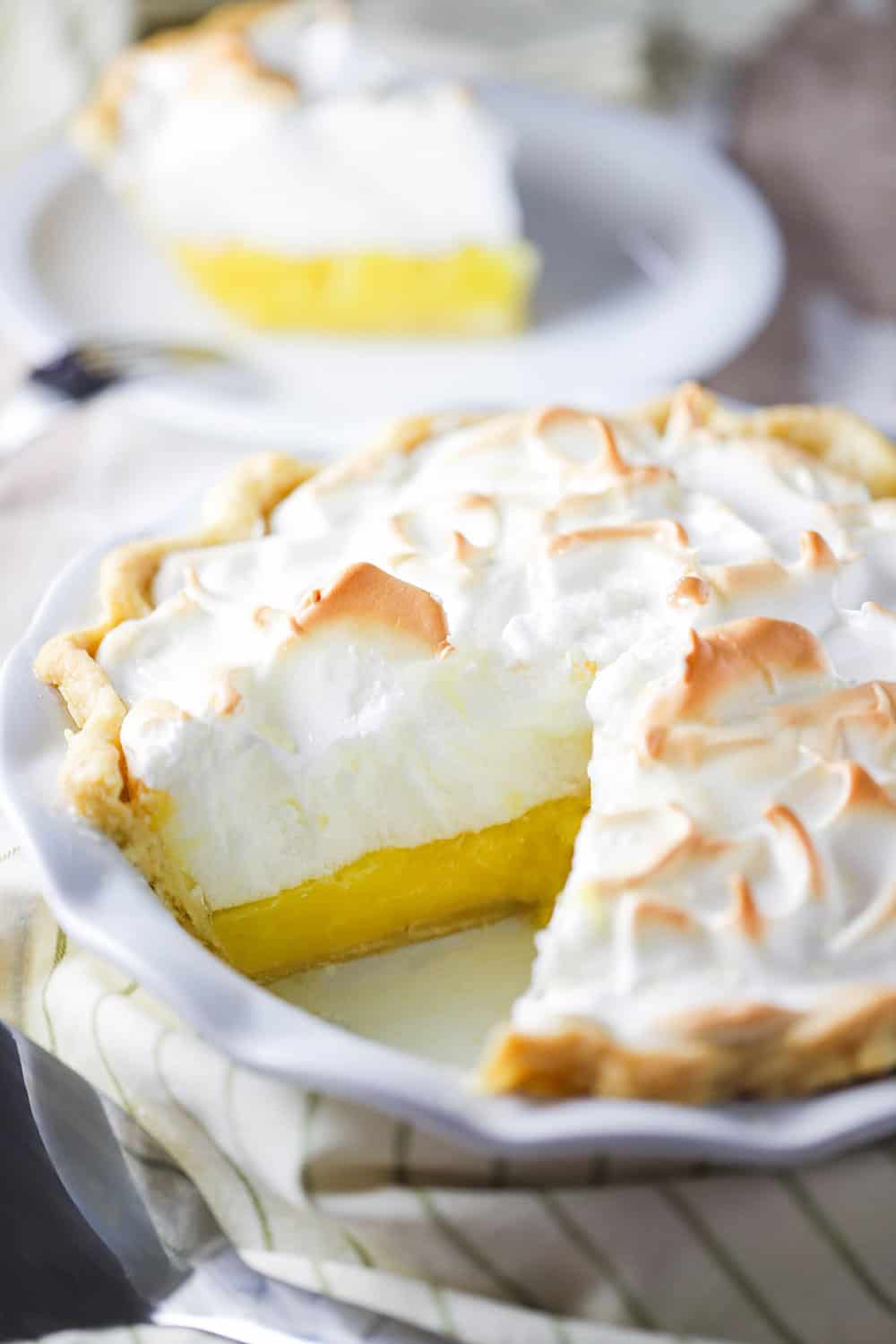 A close up view of a lemon meringue pie in a white pie dish with a slice missing.