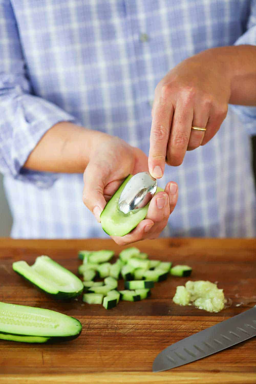 A man using a spoon to scrape the seed out of a cucumber that has been cut in half, lengthwise.