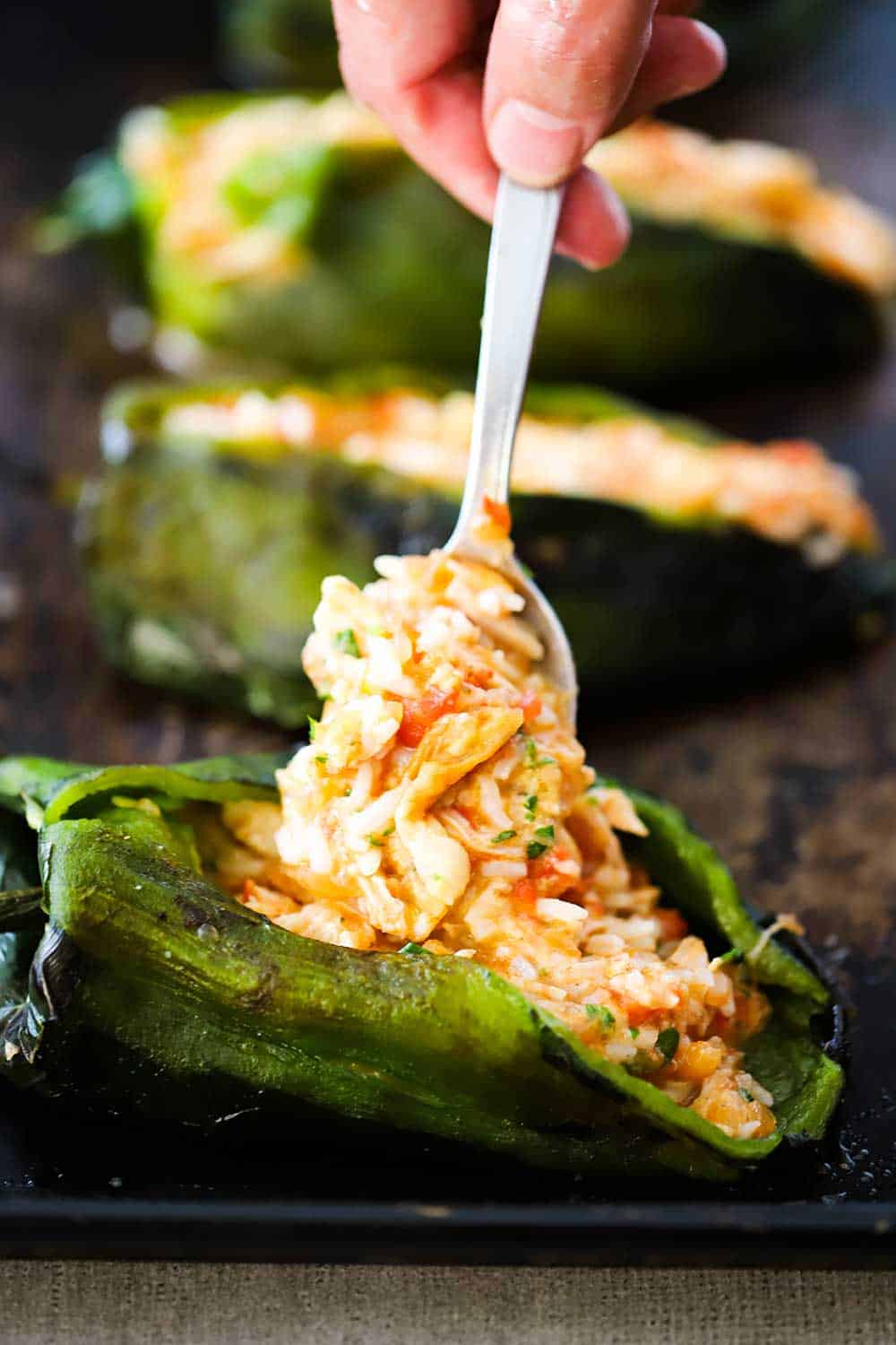 A hand using a spoon to fill a roasted poblano pepper with a chicken and rice mixture. 