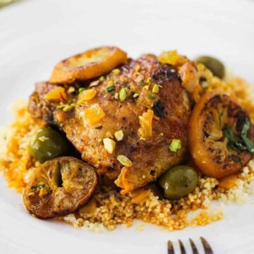 A white plate filled with chicken tagine with preserved lemons and olives with a fork resting on the plate.
