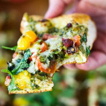 A hand holding a square piece of a BLT Pizza with a bite taken out.