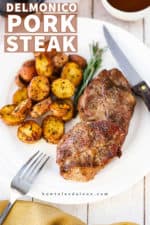 An overhead view of a white dinner plate with a grilled Delmonico pork steak on it next to a sprig of rosemary and roasted new potatoes.