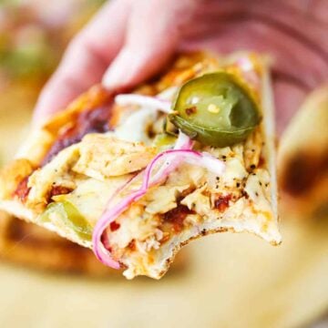A close up view of a hand holding a slice of BBQ chicken pizza with a bite taken out of it.