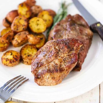 A pork burger with a sliced of green lettuce under the patty and a slice of tomato on top all on a wooden cutting board.
