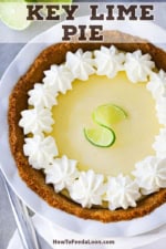 An untouched key lime pie with whipped cream pinwheels along the edge of the pie and a folded lime slice in the middle.