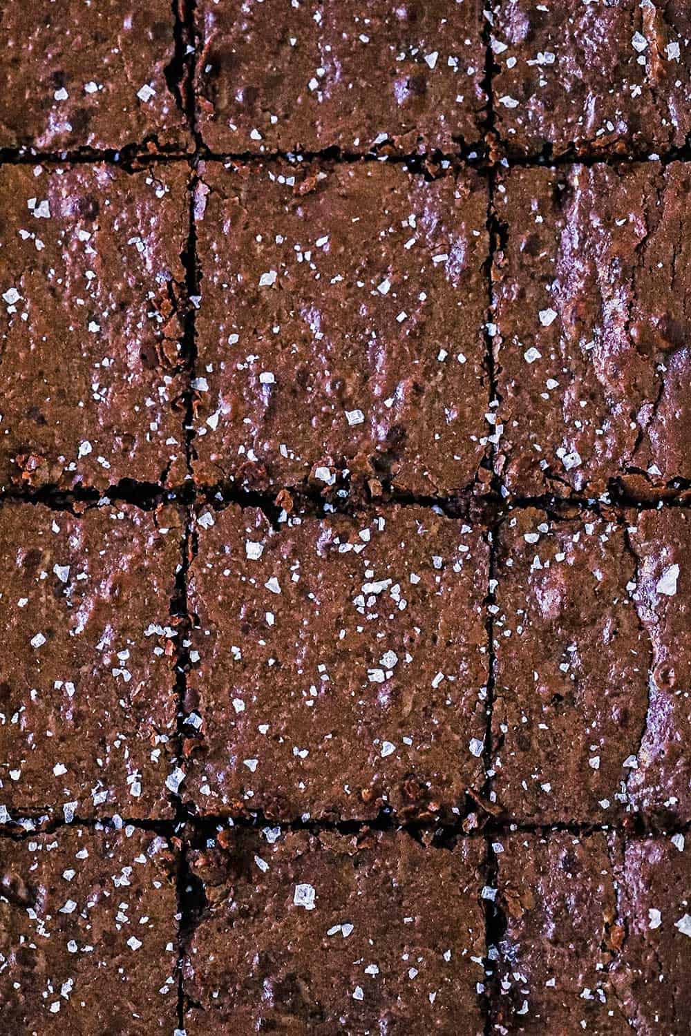 An overhead view of fudge brownies that are cut into squares and sprinkled with coarse sea salt. 