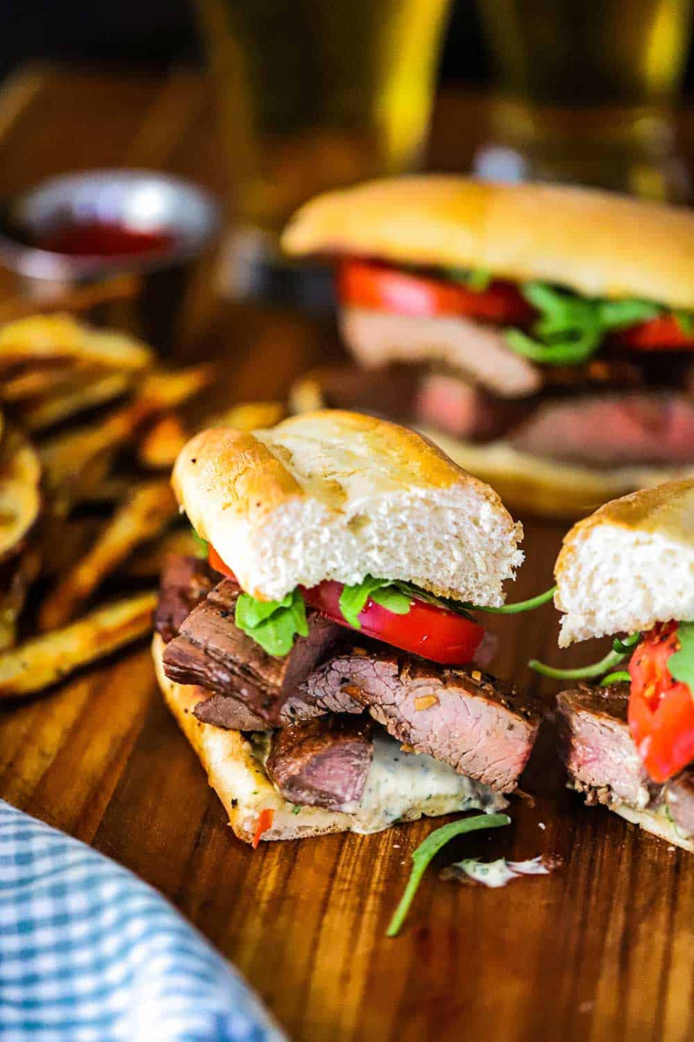 A grilled steak sandwich that has been cut in half and is sitting on a cutting board next to steak fries. 
