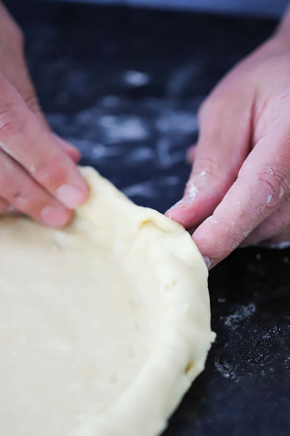 A tart pan filled with pie dough, and two hands forming a double edge of dough along the edges. 
