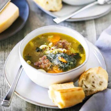 Two white soup bowls filled with Italian wedding soup on small plates with pieces of bread on them.