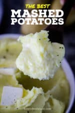 A large wooden spoon holding up a big helping of creamy mashed potatoes.