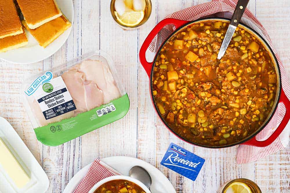 A pot of Brunswick stew sitting next to a package of air chilled chicken and a Tom Thumb card.