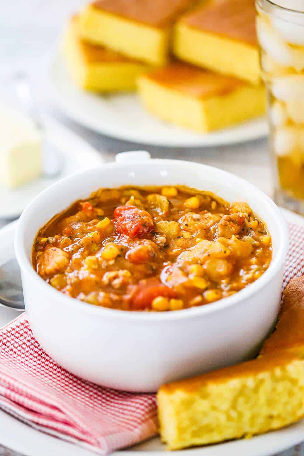 A large white soup bowl filled with Brunswick stew with a piece of cornbread next to it. 