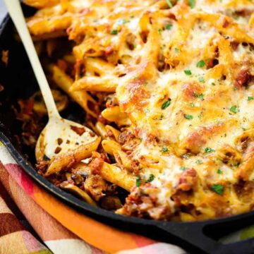 A large cast-iron skillet filled with vegetarian pasta bake with a spoon in it.