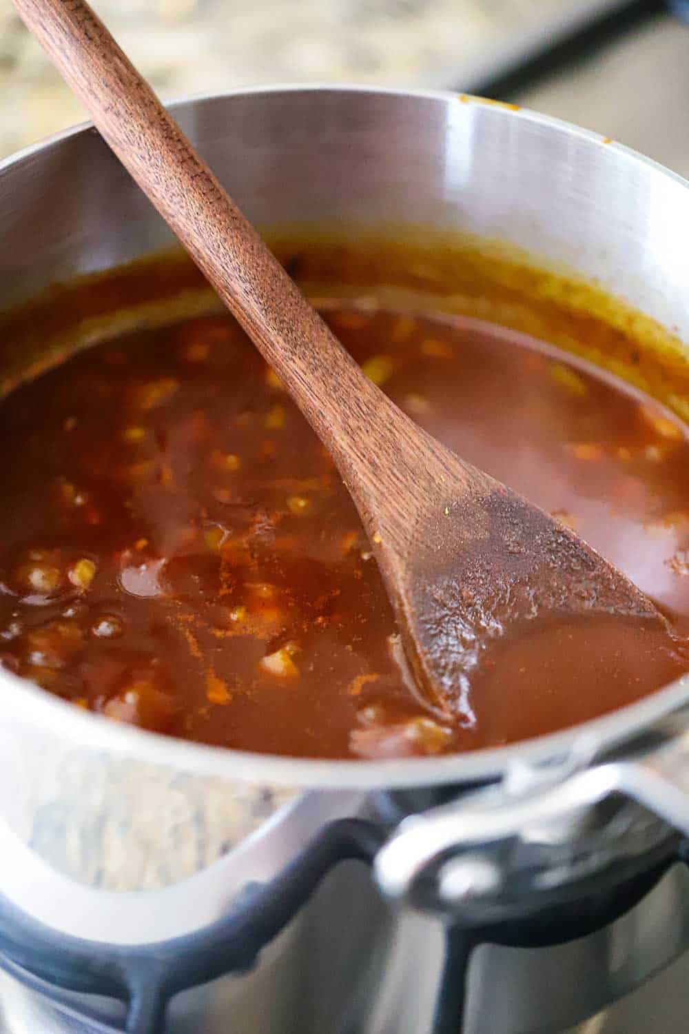 A silver saucepan filled with a BBQ sauce with a wooden spoon in it. 