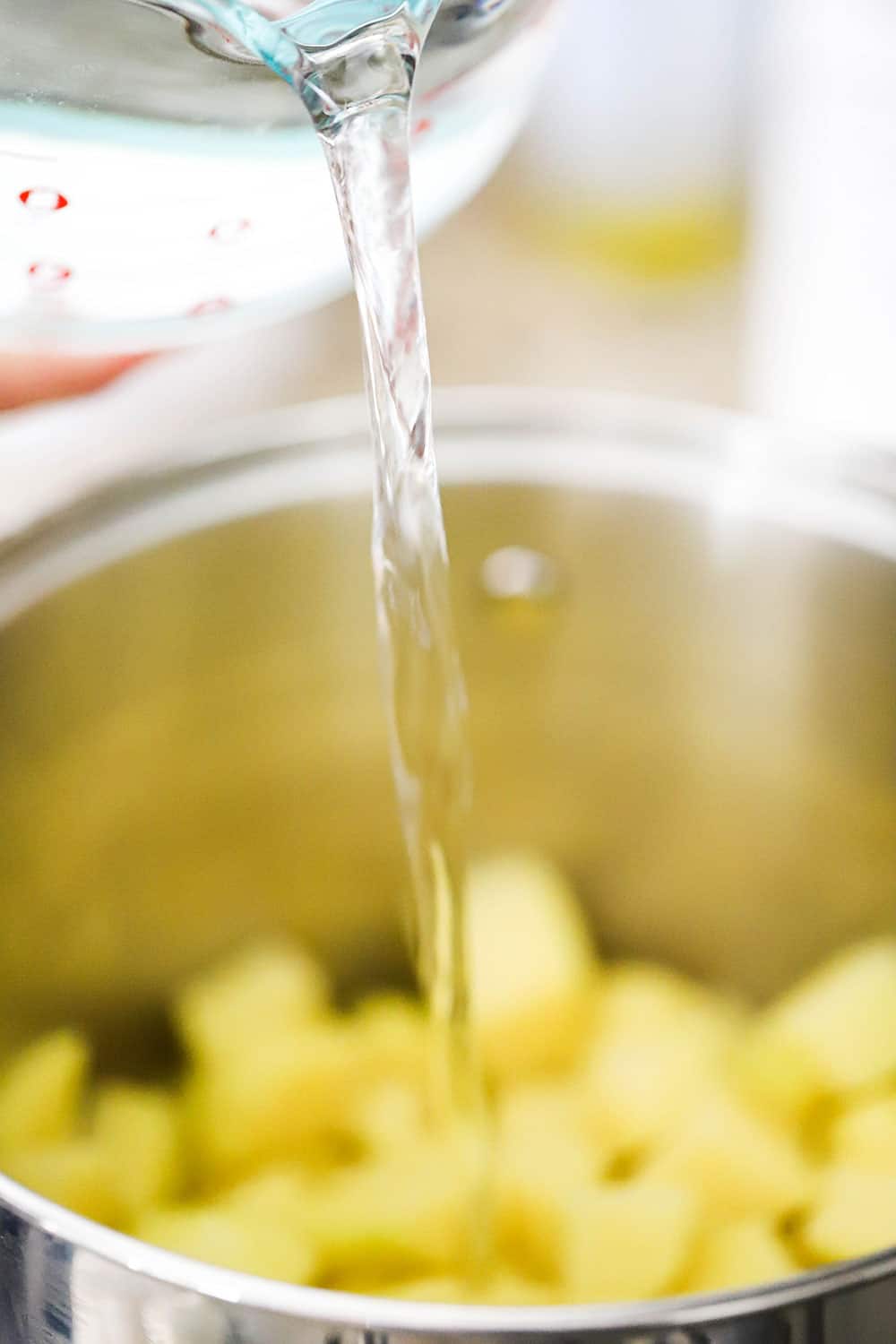 Water being poured from a 10-cup measuring cup into a pot of cubed potatoes. 