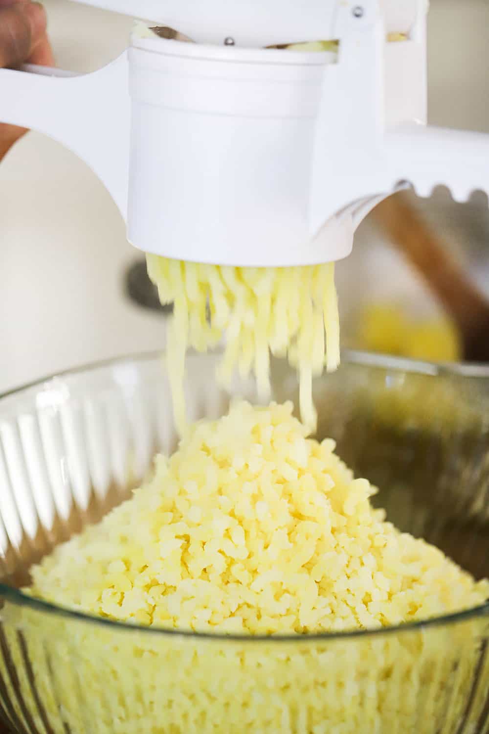 Cooked gold potatoes being passed through a ricer into a glass bowl. 